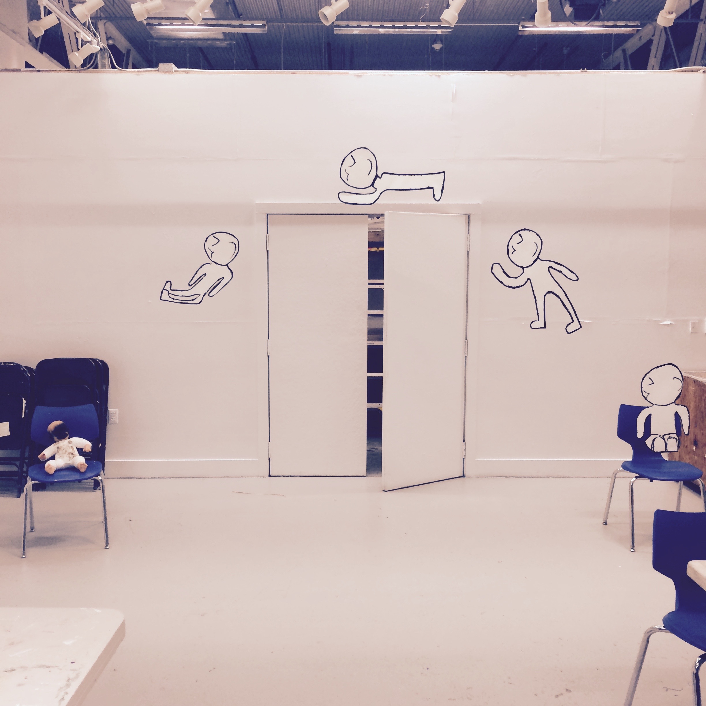 Room installation with hand-drawn figures around a doorway and dolls seated on chairs