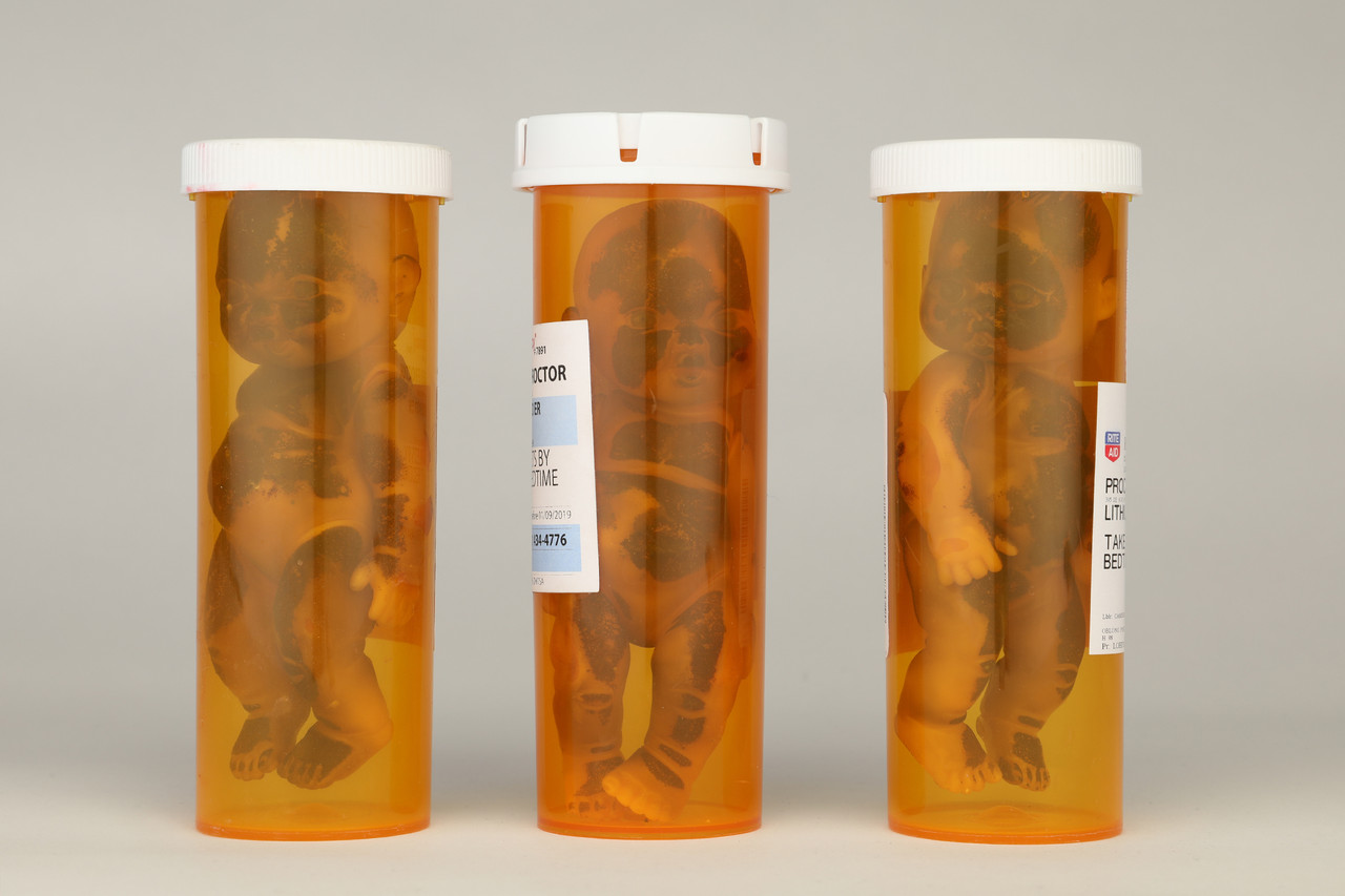 Three prescription bottles each holding a small figure suspended in amber
